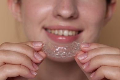 Photo of Smiling woman wearing dental aligner on beige background, selective focus