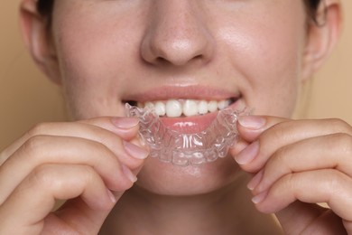 Photo of Smiling woman wearing dental aligner on beige background, closeup