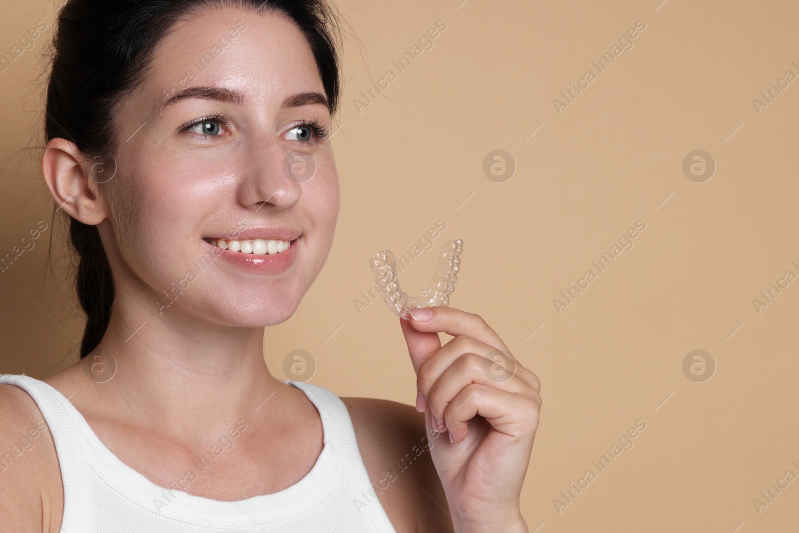 Smiling woman with dental aligner on beige background, closeup. Space for text Photo of Smiling woman with dental aligner on beige background, closeup. Space for text