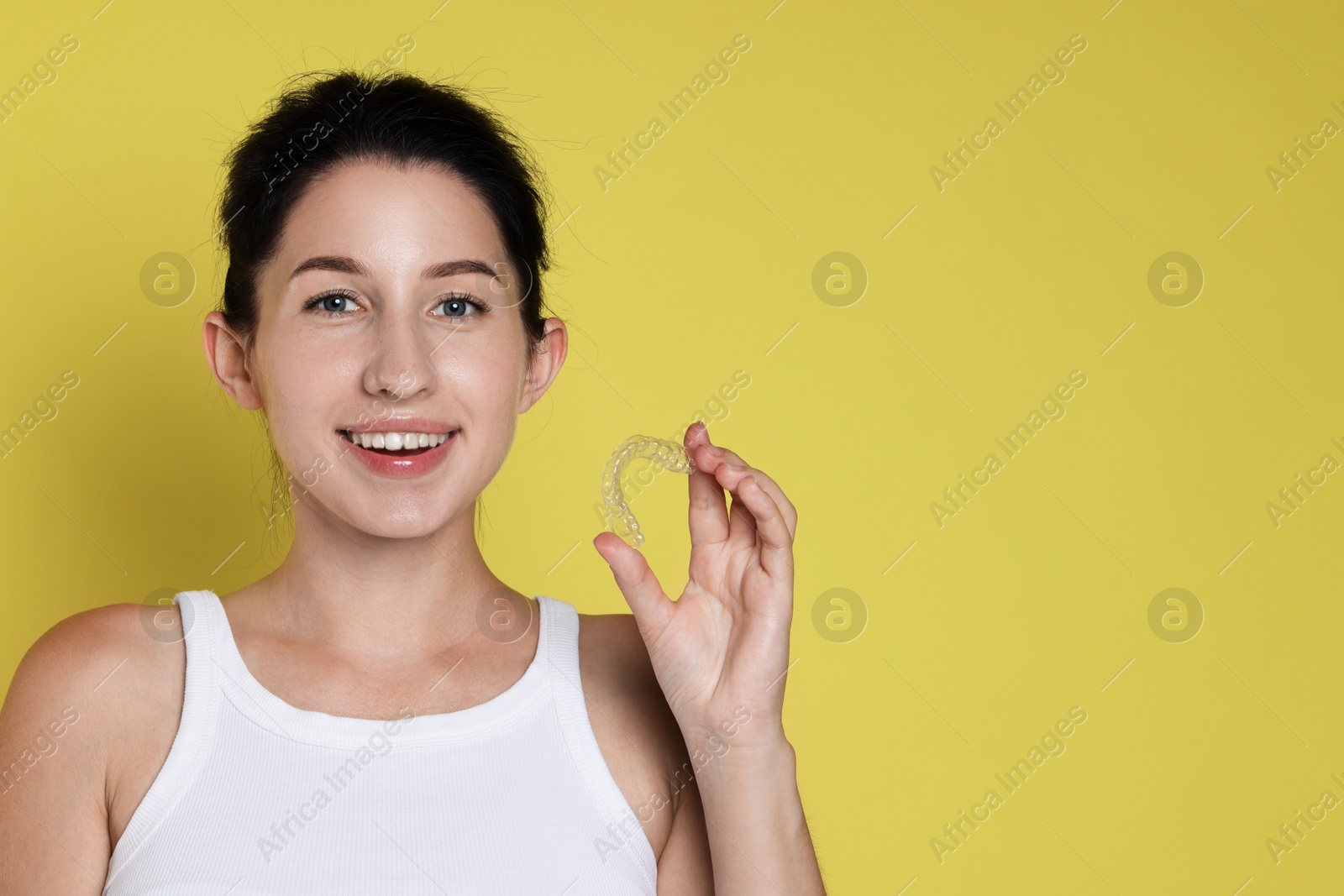 Smiling woman with dental aligner on yellow background. Space for text Photo of Smiling woman with dental aligner on yellow background. Space for text