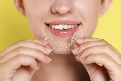 Photo of Smiling woman with dental aligner on yellow background, closeup
