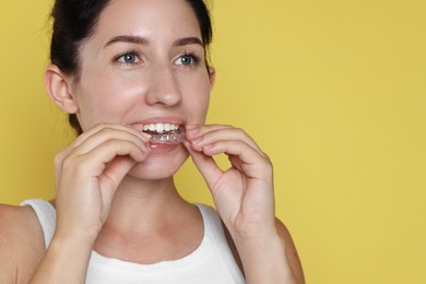 Photo of Beautiful woman wearing dental aligner on yellow background, closeup. Space for text