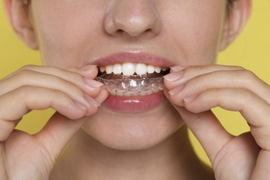 Photo of Woman wearing dental aligner on yellow background, closeup