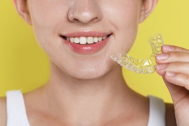 Photo of Smiling woman with dental aligner on yellow background, closeup