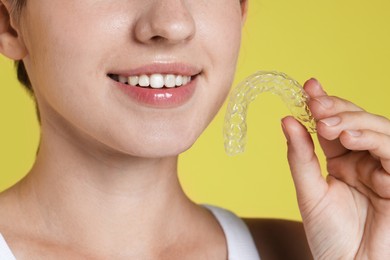 Photo of Smiling woman with dental aligner on yellow background, closeup
