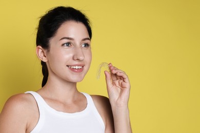 Photo of Smiling woman with dental aligner on yellow background. Space for text