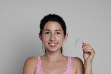 Photo of Portrait of smiling woman with dental aligner on grey background