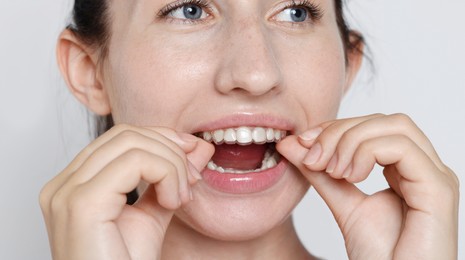 Photo of Woman wearing dental aligner on grey background, closeup