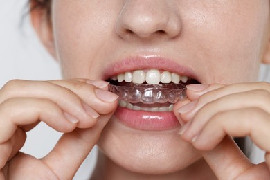 Photo of Woman wearing dental aligner on grey background, closeup