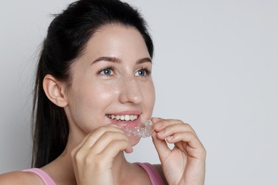 Photo of Smiling woman wearing dental aligner on grey background, closeup