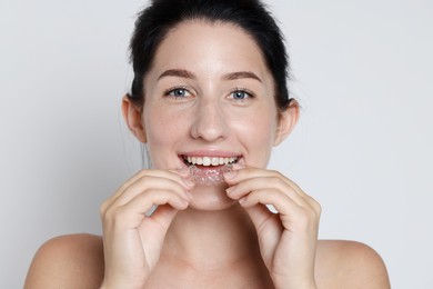 Photo of Portrait of smiling woman wearing dental aligner on grey background, closeup