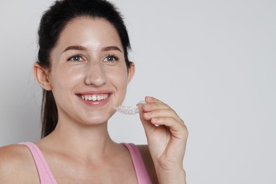 Photo of Smiling woman with dental aligner on grey background, closeup. Space for text