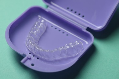 Photo of Clear aligner in retainer case on turquoise background, closeup