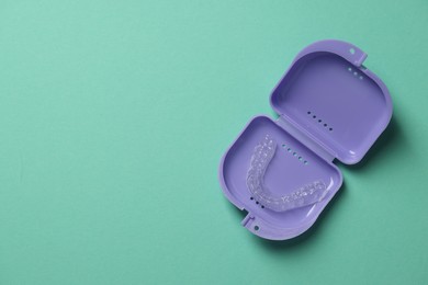 Photo of Clear aligner in retainer case on turquoise background, top view. Space for text