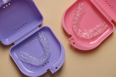 Photo of Clear aligners in colorful retainer cases on beige background, flat lay