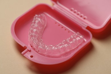Photo of Clear aligner in retainer case on beige background, closeup
