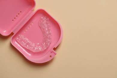 Photo of Clear aligner in retainer case on beige background, top view. Space for text
