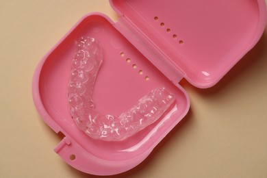 Photo of Clear aligner in retainer case on beige background, top view