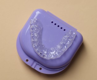 Photo of Clear aligner in retainer case on beige background, top view