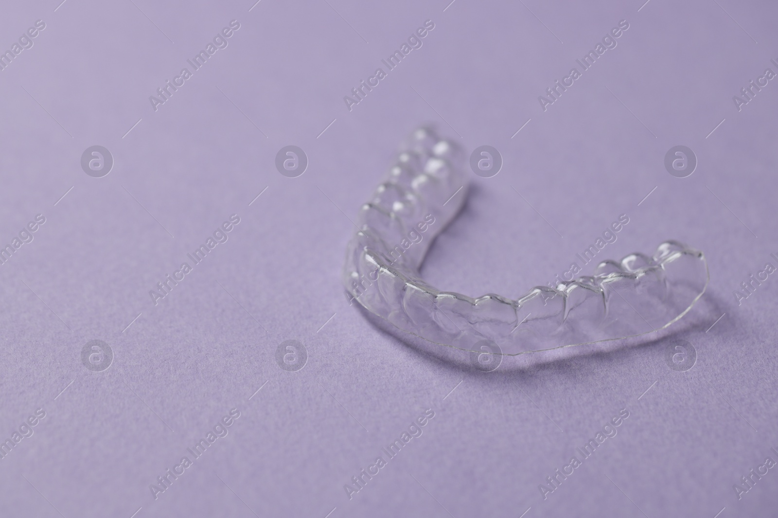 One clear aligner on violet background, closeup. Space for text Photo of One clear aligner on violet background, closeup. Space for text