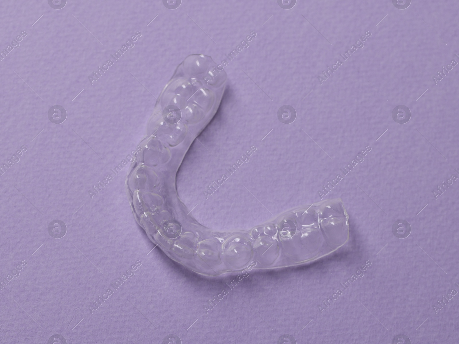 One clear aligner on violet background, top view Photo of One clear aligner on violet background, top view