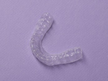 Photo of One clear aligner on violet background, top view