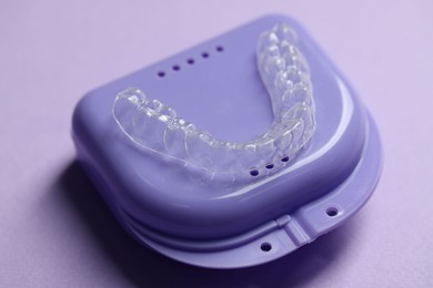 Photo of One clear aligner and retainer case on violet background, closeup