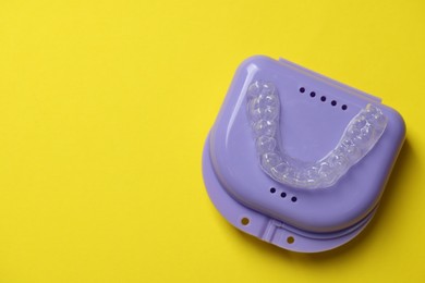 Photo of One clear aligner and retainer case on yellow background, top view. Space for text