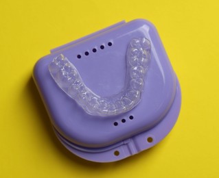 Photo of One clear aligner and retainer case on yellow background, top view