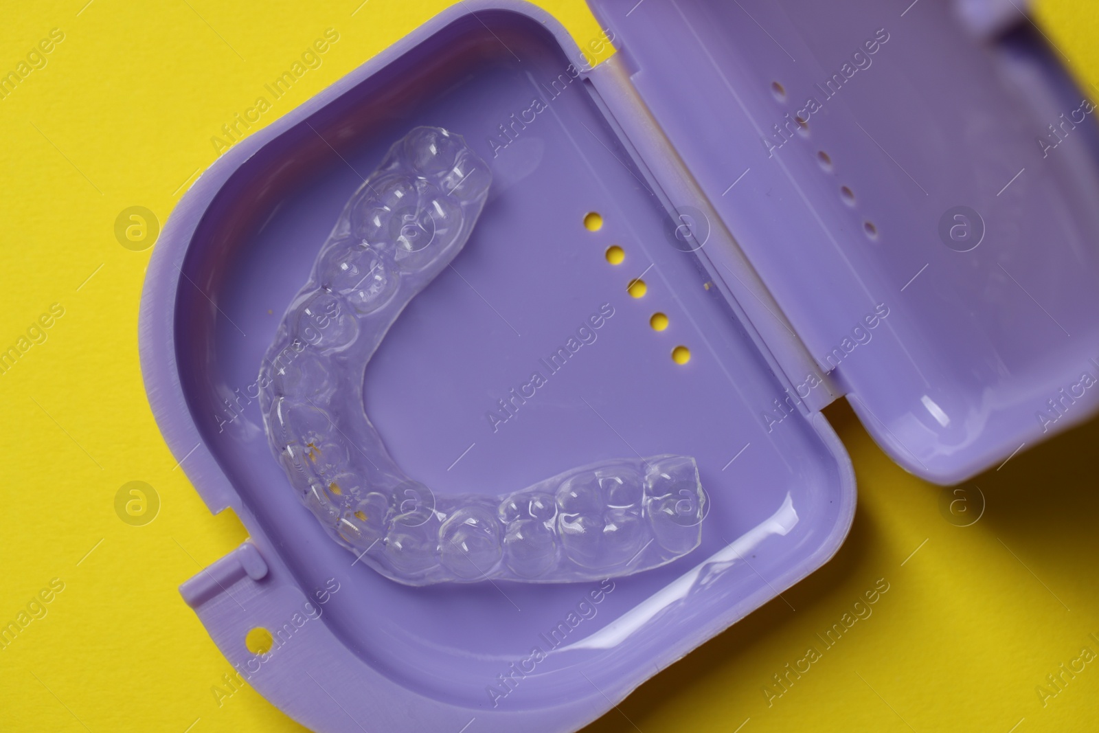 One clear aligner in retainer case on yellow background, top view Photo of One clear aligner in retainer case on yellow background, top view