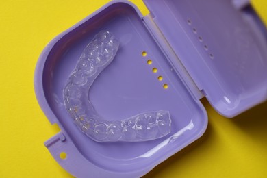 Photo of One clear aligner in retainer case on yellow background, top view