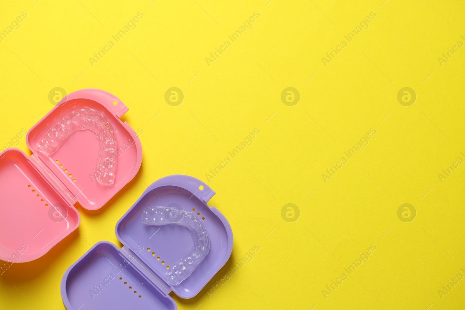 Clear aligners in colorful retainer cases on yellow background, flat lay. Space for text Photo of Clear aligners in colorful retainer cases on yellow background, flat lay. Space for text