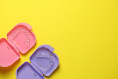 Photo of Clear aligners in colorful retainer cases on yellow background, flat lay. Space for text