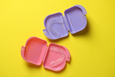 Photo of Clear aligners in colorful retainer cases on yellow background, flat lay