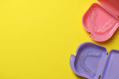 Photo of Clear aligners in colorful retainer cases on yellow background, flat lay. Space for text