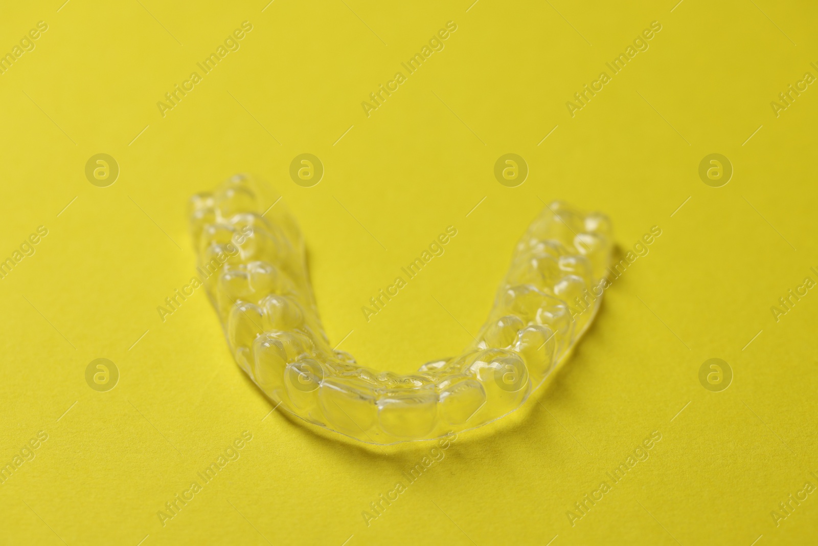 One clear aligner on yellow background, closeup Photo of One clear aligner on yellow background, closeup
