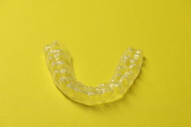 Photo of One clear aligner on yellow background, closeup