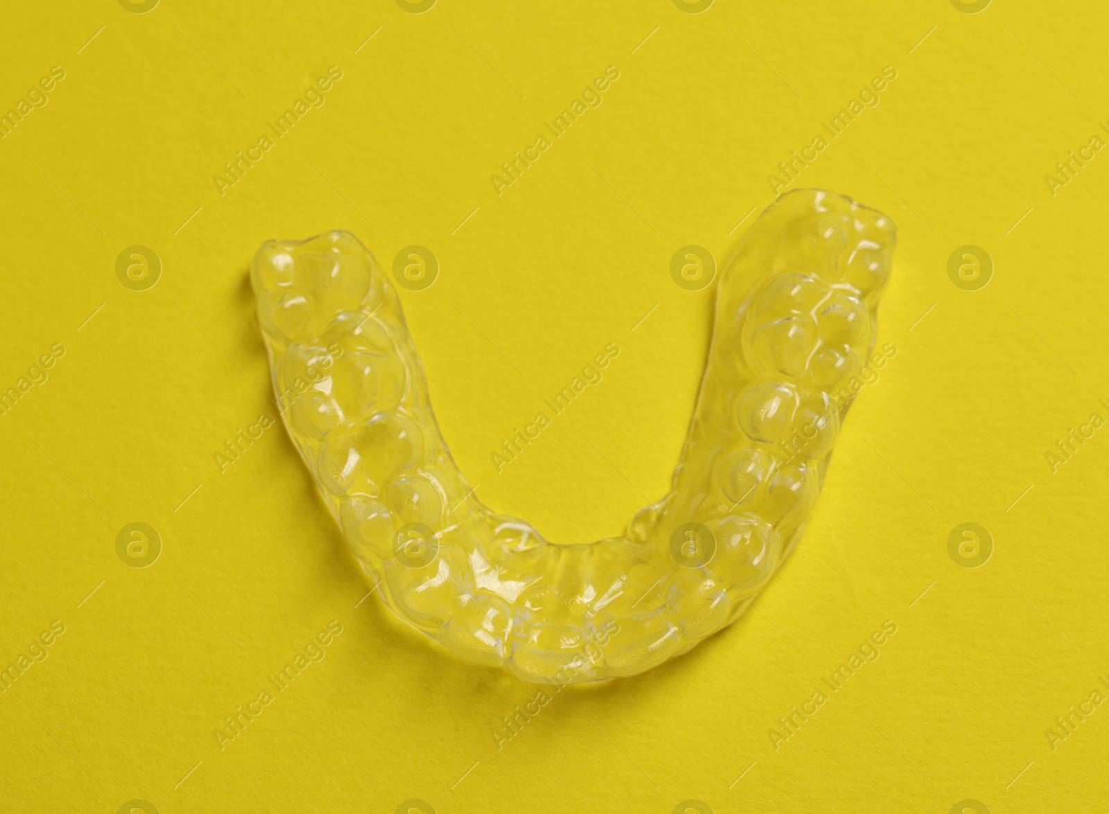 One clear aligner on yellow background, top view Photo of One clear aligner on yellow background, top view