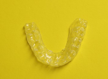 Photo of One clear aligner on yellow background, top view
