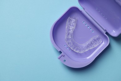 Photo of One clear aligner in retainer case on light blue background, top view. Space for text