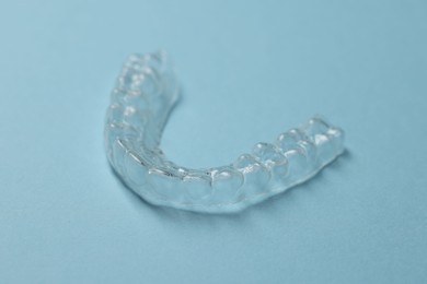 Photo of One clear aligner on light blue background, closeup