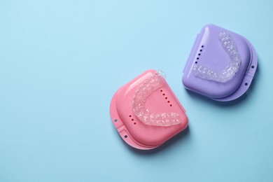 Photo of Clear aligners and colorful retainer cases on light blue background, flat lay. Space for text