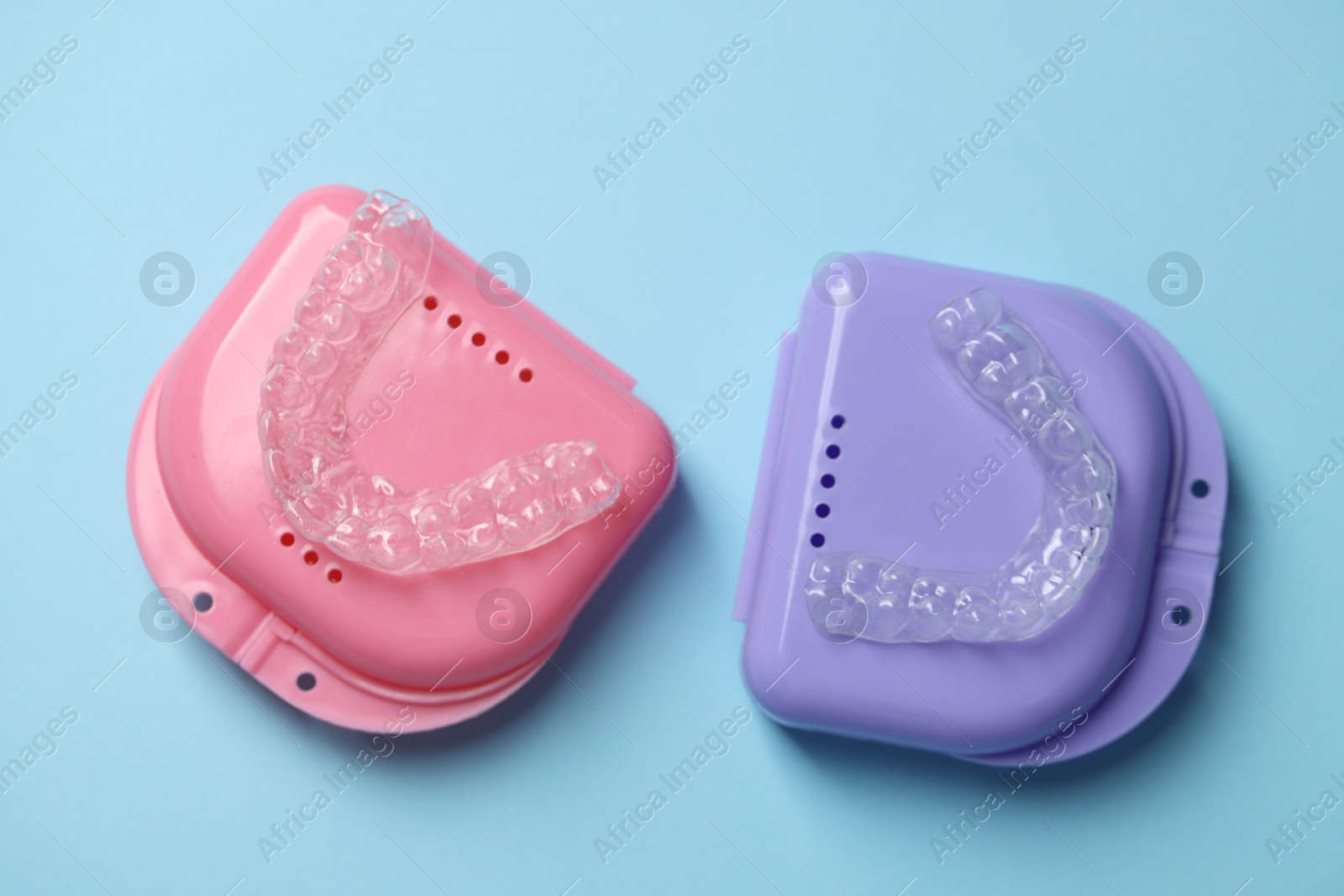 Clear aligners and colorful retainer cases on light blue background, flat lay Photo of Clear aligners and colorful retainer cases on light blue background, flat lay