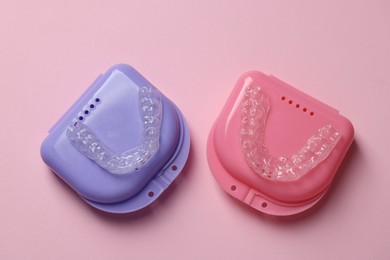 Photo of Clear aligners and colorful retainer cases on pink background, flat lay
