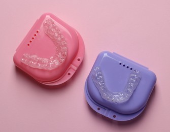 Photo of Clear aligners and colorful retainer cases on pink background, flat lay