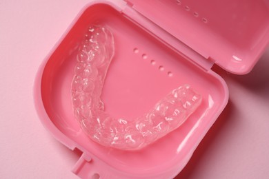 Photo of One clear aligner in retainer case on pink background, top view