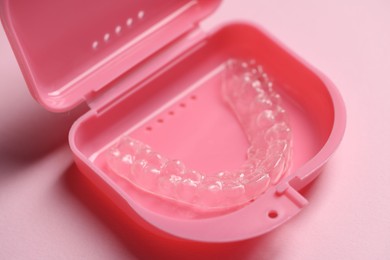 Photo of One clear aligner in retainer case on pink background, closeup