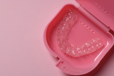 Photo of One clear aligner in retainer case on pink background, top view. Space for text