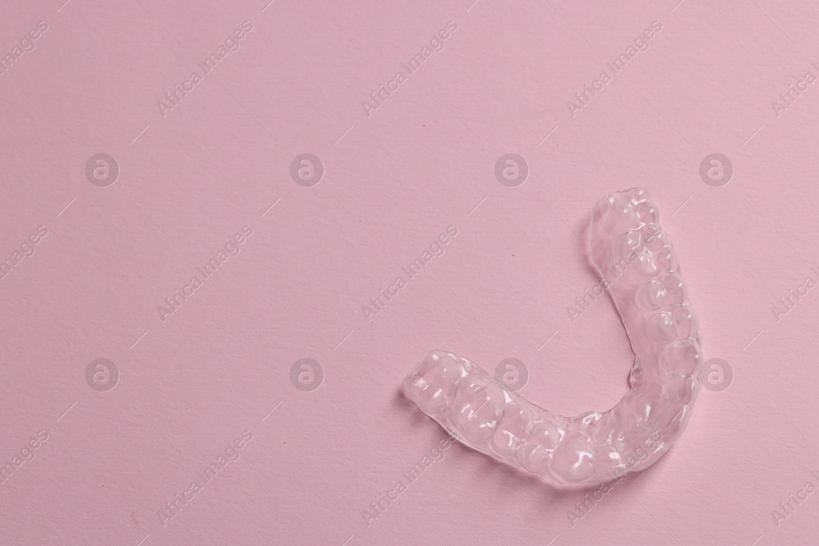 One clear aligner on pink background, top view. Space for text Photo of One clear aligner on pink background, top view. Space for text