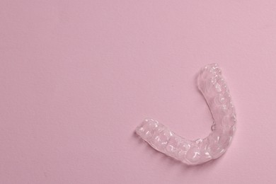 Photo of One clear aligner on pink background, top view. Space for text